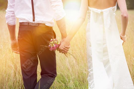 A bride and groom holding hands in a sunny meadow, with the groom carrying a small bouquet of wildflowers, symbolizing love, romance, and the beginning of a new journey together  : Stock Photo or Stock Video Download rcfotostock photos, images and assets rcfotostock | RC Photo Stock.: