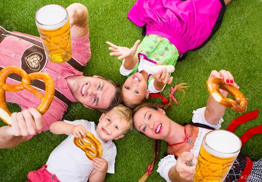 A cheerful family in traditional Bavarian attire, lying on grass, holding pretzels, beer, and sausages, celebrating Oktoberfest with bright smiles, joy, and a festive atmosphere  : Stock Photo or Stock Video Download rcfotostock photos, images and assets rcfotostock | RC Photo Stock.: