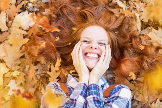 A cheerful red-haired woman lying in a pile of autumn leaves, smiling brightly, with her hair spread out and hands on her cheeks, surrounded by warm fall colors  : Stock Photo or Stock Video Download rcfotostock photos, images and assets rcfotostock | RC Photo Stock.: