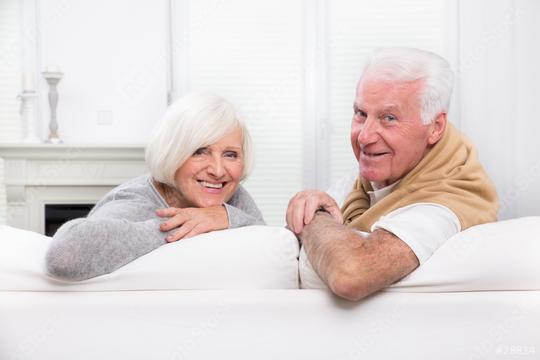A cheerful senior couple relaxing on a white sofa in a bright and cozy living room, smiling warmly and enjoying a moment of connection and companionship in a peaceful home setting  : Stock Photo or Stock Video Download rcfotostock photos, images and assets rcfotostock | RC Photo Stock.: