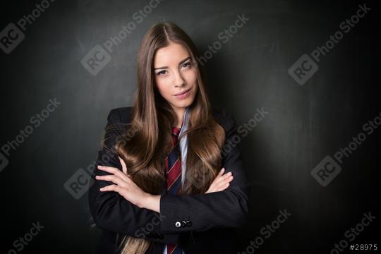 A confident young woman with long brown hair wearing a formal suit and tie, standing with folded arms in front of a blackboard, exuding professionalism and determination  : Stock Photo or Stock Video Download rcfotostock photos, images and assets rcfotostock | RC Photo Stock.: