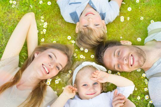 A happy family of four lies on the grass surrounded by daisies, smiling and enjoying quality time outdoors, creating a moment of togetherness, relaxation, and nature bonding  : Stock Photo or Stock Video Download rcfotostock photos, images and assets rcfotostock | RC Photo Stock.: