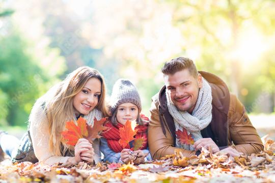 A happy family of three lying on colorful autumn leaves in a sunny park, holding vibrant red and orange leaves, dressed warmly with scarves and hats, enjoying quality time together in nature  : Stock Photo or Stock Video Download rcfotostock photos, images and assets rcfotostock | RC Photo Stock.: