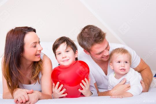 A happy family spending quality time together on a bed, with a young boy holding a large red heart, symbolizing love, bonding, and warmth in a cozy indoor setting  : Stock Photo or Stock Video Download rcfotostock photos, images and assets rcfotostock | RC Photo Stock.: