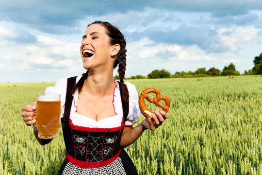 A joyful woman in traditional Bavarian dress holds a mug of beer and a pretzel, laughing in a lush green field under a bright sky, celebrating culture and festivity.  : Stock Photo or Stock Video Download rcfotostock photos, images and assets rcfotostock | RC Photo Stock.: