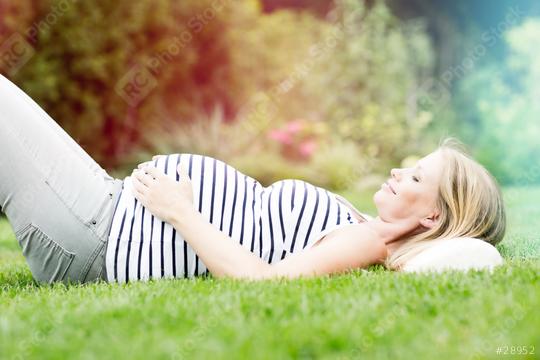 A pregnant woman lies on her back in a grassy garden, wearing a striped tank top, with her hands on her belly, enjoying the peaceful and relaxing outdoor environment with a soft, colorful glow.  : Stock Photo or Stock Video Download rcfotostock photos, images and assets rcfotostock | RC Photo Stock.: