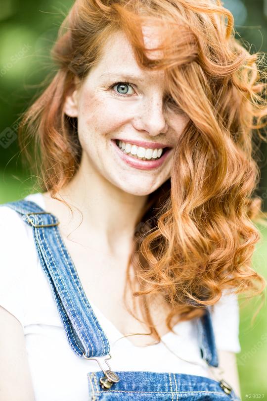 A red-haired woman with curly hair and a bright smile wearing denim overalls, captured outdoors with a lush green background, radiating natural beauty and joy  : Stock Photo or Stock Video Download rcfotostock photos, images and assets rcfotostock | RC Photo Stock.: