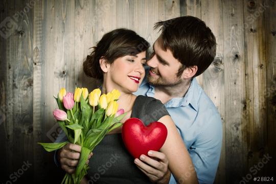 A romantic couple embraces with smiles, holding a bouquet of tulips and a red heart against a rustic wooden backdrop, symbolizing love, affection, and connection  : Stock Photo or Stock Video Download rcfotostock photos, images and assets rcfotostock | RC Photo Stock.: