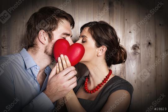 A romantic couple sharing a kiss while holding a red heart together in front of them, set against a rustic wooden background, symbolizing love, intimacy, and a special connection  : Stock Photo or Stock Video Download rcfotostock photos, images and assets rcfotostock | RC Photo Stock.: