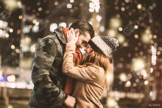 A romantic couple sharing an intimate moment outdoors on a winter night with warm clothing, festive lights, and a cozy atmosphere filled with bokeh  : Stock Photo or Stock Video Download rcfotostock photos, images and assets rcfotostock | RC Photo Stock.: