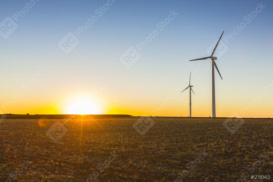 A scenic view of two wind turbines standing tall in an open field during sunset, with golden sunlight casting a warm glow over the landscape and a clear sky transitioning into dusk  : Stock Photo or Stock Video Download rcfotostock photos, images and assets rcfotostock | RC Photo Stock.: