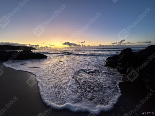 A serene beach at sunset with gentle waves washing onto the shore, framed by dark rocks and a colorful sky transitioning from blue to orange.
  : Stock Photo or Stock Video Download rcfotostock photos, images and assets rcfotostock | RC Photo Stock.: