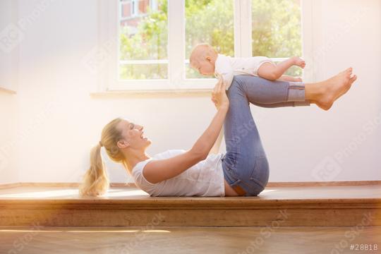 A smiling mother plays with her baby in a bright, sunlit room, holding the child up with her legs in a playful pose near a large window  : Stock Photo or Stock Video Download rcfotostock photos, images and assets rcfotostock | RC Photo Stock.:
