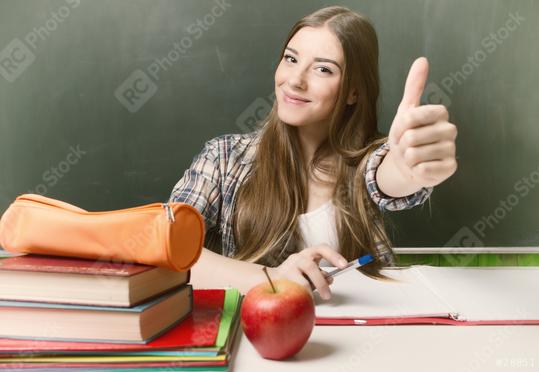 A smiling student gives a thumbs-up in front of a chalkboard with books, a pen, an orange pencil case, and an apple on the desk, symbolizing education, positivity, and learning success  : Stock Photo or Stock Video Download rcfotostock photos, images and assets rcfotostock | RC Photo Stock.: