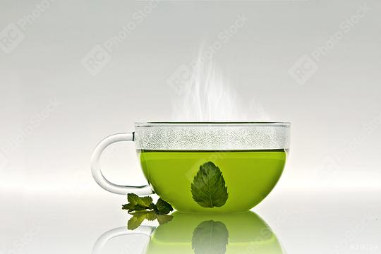 A steaming glass cup of green tea with a mint leaf inside and a few fresh mint leaves placed beside it on a reflective surface  : Stock Photo or Stock Video Download rcfotostock photos, images and assets rcfotostock | RC Photo Stock.: