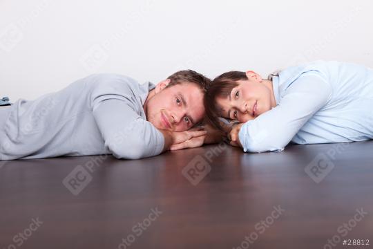 A young couple lying on a dark wooden floor, resting their heads on their hands, gazing forward with relaxed and thoughtful expressions in a minimalist indoor setting  : Stock Photo or Stock Video Download rcfotostock photos, images and assets rcfotostock | RC Photo Stock.: