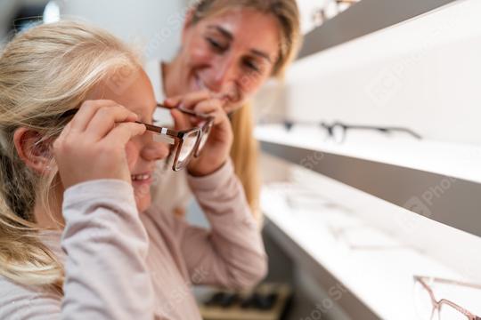 Adult assisting a child in trying on new eyeglasses at a optical store  : Stock Photo or Stock Video Download rcfotostock photos, images and assets rcfotostock | RC Photo Stock.: