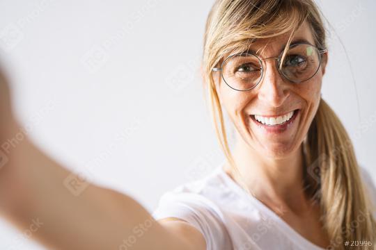 Attractive blonde woman dressed casually and glasses look smiling broadly. Beautiful woman having cheerful expression while posing against white background, stretching arm to camera for a selfie  : Stock Photo or Stock Video Download rcfotostock photos, images and assets rcfotostock | RC Photo Stock.: