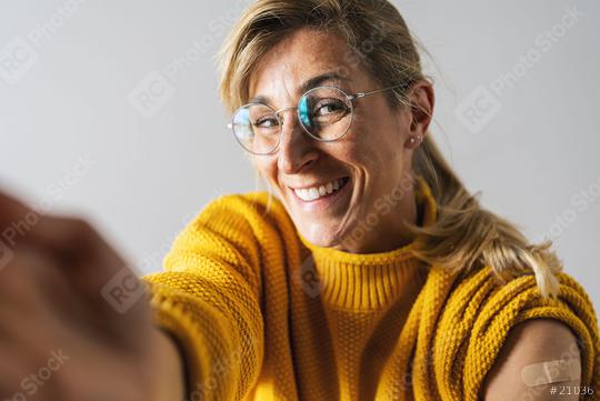 Attractive mature woman smiling after getting a corona vaccine. Woman holding up her shirt sleeve and showing her arm with bandage after receiving vaccination, stretching arm to camera for a selfie.  : Stock Photo or Stock Video Download rcfotostock photos, images and assets rcfotostock | RC Photo Stock.: