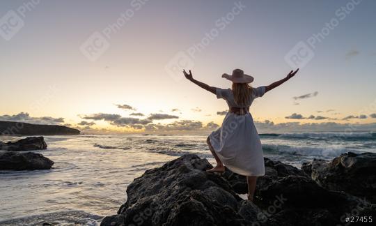 Back view of a woman in a white dress and straw hat with arms raised, standing on rocks at sunset by the ocean  : Stock Photo or Stock Video Download rcfotostock photos, images and assets rcfotostock | RC Photo Stock.: