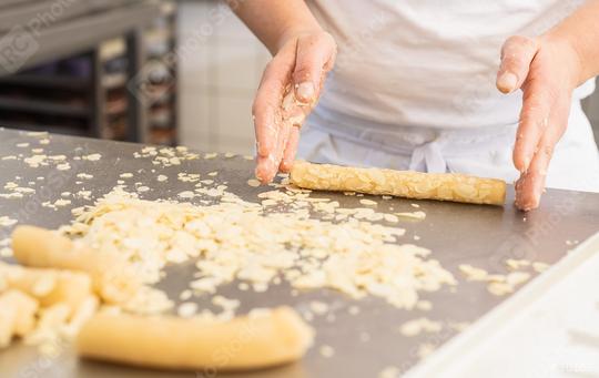 Baker rolling cookie dough in almond slices on a work surface in a bakery, preparing the dough for baking with hands covered in almond flakes in a professional baking environment  : Stock Photo or Stock Video Download rcfotostock photos, images and assets rcfotostock | RC Photo Stock.: