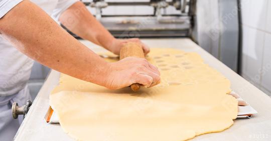 baker rolls out cookie dough on a work surface using a wooden rolling pin, preparing it for cutting shapes. The scene captures the hands-on baking process in a professional kitchen  : Stock Photo or Stock Video Download rcfotostock photos, images and assets rcfotostock | RC Photo Stock.: