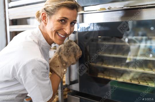 baker smiles while checking on the baking cookies through the oven door, wearing a glove for safety. The scene captures the joy and dedication involved in baking.  : Stock Photo or Stock Video Download rcfotostock photos, images and assets rcfotostock | RC Photo Stock.: