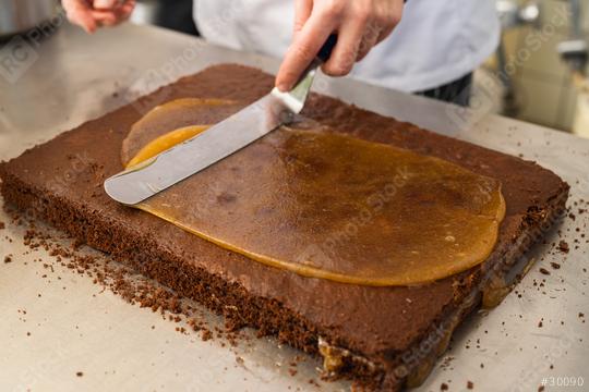 Baker spreading caramel on a chocolate cake layer using a spatula in a bakery, preparing the cake for layering in a professional baking environment  : Stock Photo or Stock Video Download rcfotostock photos, images and assets rcfotostock | RC Photo Stock.:
