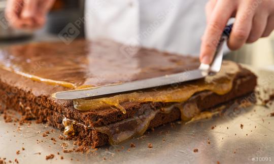 Baker spreading caramel on a chocolate cake layer with a spatula in a bakery, carefully smoothing the filling in preparation for the next layer in a professional baking environment  : Stock Photo or Stock Video Download rcfotostock photos, images and assets rcfotostock | RC Photo Stock.: