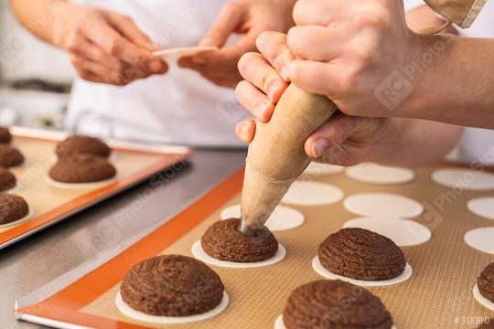 baker uses a piping bag to pipe gingerbread dough onto wafers on a baking sheet, while another baker prepares more wafers, in a professional kitchen setting  : Stock Photo or Stock Video Download rcfotostock photos, images and assets rcfotostock | RC Photo Stock.: