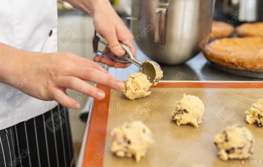 baker uses a scoop to portion cookie dough onto a baking sheet, preparing the cookies for baking. The scene captures the precision and care in the baking process.  : Stock Photo or Stock Video Download rcfotostock photos, images and assets rcfotostock | RC Photo Stock.: