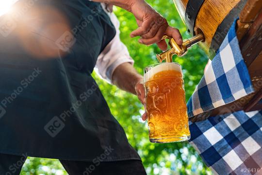 Bavarian man in apron is pouring a large lager beer in tap from wooden beer barrel in the beer garden. Background for Oktoberfest, folk or beer festival (German for: O’zapft is!)   : Stock Photo or Stock Video Download rcfotostock photos, images and assets rcfotostock | RC Photo Stock.: