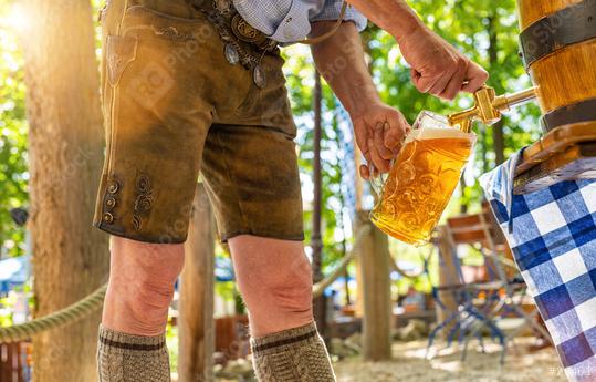 Bavarian man in leather trousers is pouring a large lager beer in tap from wooden beer barrel in the beer garden. Background for Oktoberfest or Wiesn, folk or beer festival  : Stock Photo or Stock Video Download rcfotostock photos, images and assets rcfotostock | RC Photo Stock.: