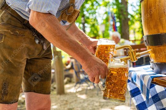 Bavarian man in leather trousers is pouring large lager beers in tap from wooden beer barrel in the beer garden. Background for Oktoberfest or Wiesn, folk or beer festival (German for: O’zapft is!)   : Stock Photo or Stock Video Download rcfotostock photos, images and assets rcfotostock | RC Photo Stock.: