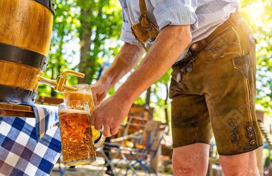 Bavarian man in traditional leather trousers is pouring large lager beers in tap from wooden beer barrel in the beer garden. Background for Oktoberfest or Wiesn, folk or beer festival   : Stock Photo or Stock Video Download rcfotostock photos, images and assets rcfotostock | RC Photo Stock.: