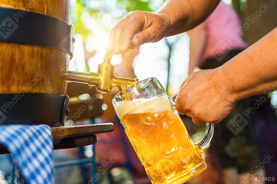 Bavarian Waitress in Tracht, Dirndl  is pouring a large lager beer in tap from wooden beer barrel in the beer garden. Background for Oktoberfest, folk or beer festival (German for: O’zapft is!)   : Stock Photo or Stock Video Download rcfotostock photos, images and assets rcfotostock | RC Photo Stock.: