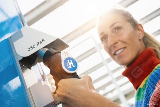beautiful woman smiling and looking away, holds a fuel dispenser with hydrogen logo on gas station to fill up her car. h2 combustion engine for emission free eco friendly transport concept image  : Stock Photo or Stock Video Download rcfotostock photos, images and assets rcfotostock | RC Photo Stock.: