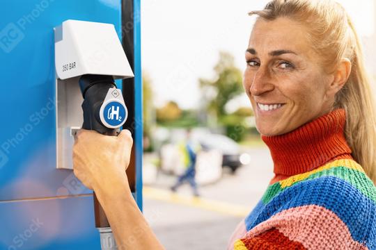 beautiful woman smiling, holds a fuel dispenser with hydrogen logo on gas station to fill up her car. h2 combustion engine for emission free eco friendly transport concept image  : Stock Photo or Stock Video Download rcfotostock photos, images and assets rcfotostock | RC Photo Stock.: