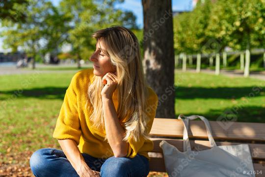 blonde woman sitting outdoor and enjoying the sun on her facce. woman relaxing on a wooden bench with fabric bag under the tree in a summer day. Portrait of woman smiling and daydreaming.  : Stock Photo or Stock Video Download rcfotostock photos, images and assets rcfotostock | RC Photo Stock.:
