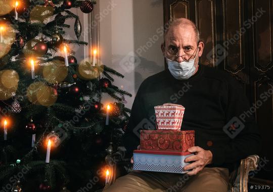 Caucasian Senior man wearing covid-19 mask sitting on chair alone holding a gift in Christmas decorated room .   : Stock Photo or Stock Video Download rcfotostock photos, images and assets rcfotostock | RC Photo Stock.: