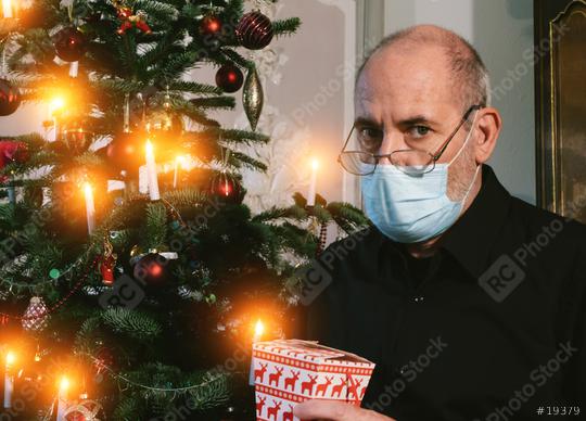 Caucasian Senior man wearing covid-19 mask sitting on chair alone holding a gift in Christmas decorated room .   : Stock Photo or Stock Video Download rcfotostock photos, images and assets rcfotostock | RC Photo Stock.: