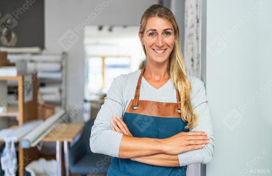 cheerful blonde woman with arms crossed in apron stands  in a tailor workspace. She has a measuring tape and a scissors in her apron pocket and is surrounded by organized craft materials   : Stock Photo or Stock Video Download rcfotostock photos, images and assets rcfotostock | RC Photo Stock.: