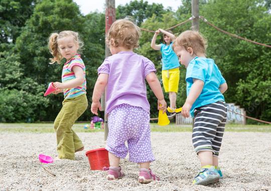Children playing outdoors in a sandbox, holding toy buckets and shovels, with a child climbing in the background, surrounded by green trees and a summer playground setting  : Stock Photo or Stock Video Download rcfotostock photos, images and assets rcfotostock | RC Photo Stock.: