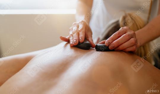 Close-up of a hot stone massage on a person’s back with therapist
