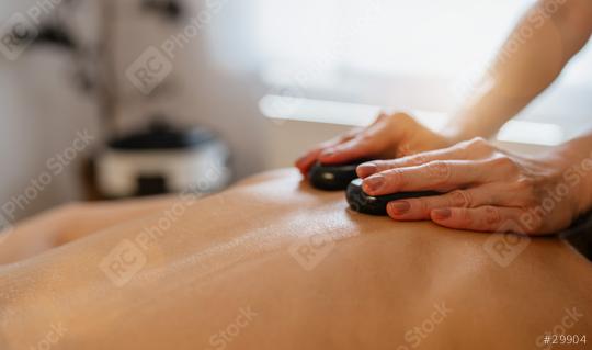 Close-up of a hot stone massage on a person’s back with therapist