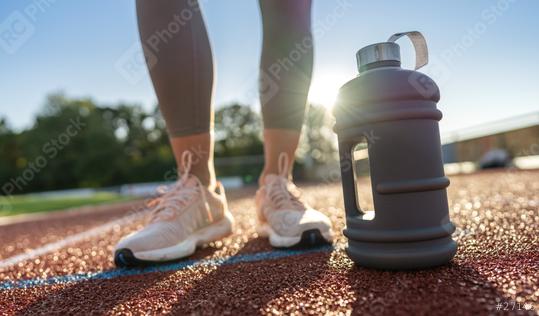 Close-up of a large water bottle on a running track with woman