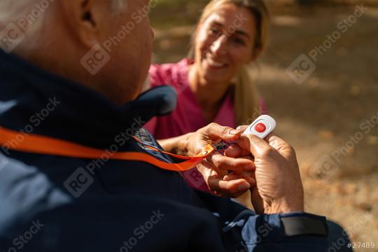 Close-up of a nurse showing an elderly man how to use an SOS button, both smiling, in a sunny park  : Stock Photo or Stock Video Download rcfotostock photos, images and assets rcfotostock | RC Photo Stock.: