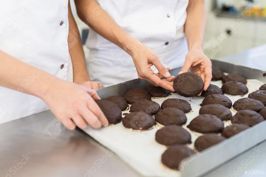 Close-up of bakers handling chocolate-covered gingerbreads on a tray in a bakery, carefully inspecting the treats in a professional baking environment  : Stock Photo or Stock Video Download rcfotostock photos, images and assets rcfotostock | RC Photo Stock.:
