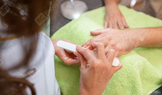 Close-up of male hands during a manicure, with a manicurist using a buffer on a client