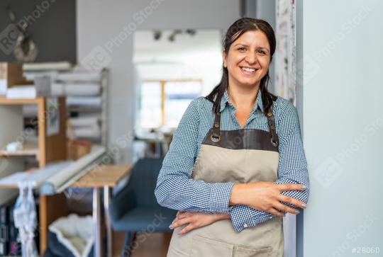 confident woman wearing a checkered shirt and beige apron stands in a workshop with folded arms, smiling towards the camera.  : Stock Photo or Stock Video Download rcfotostock photos, images and assets rcfotostock | RC Photo Stock.: